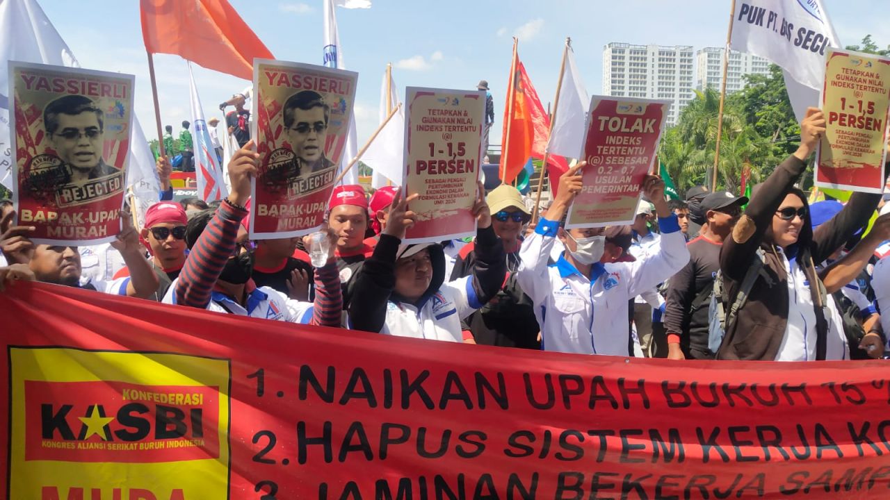 Para buruh membentangkan spanduk dan mengangkat poster Berisi tuntutan mereka